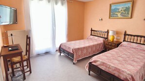 Hotellihuone, jossa on kaksi erillistä sänkyä, työpöytä tuolilla, punainen nojatuoli, televisio ja taulu seinällä.