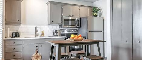 Una cocina moderna con armarios grises, electrodomésticos de acero inoxidable, una mesa de madera con taburetes y un frutero.
