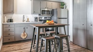 Una cocina moderna con armarios grises, electrodomésticos de acero inoxidable, una mesa de madera con taburetes y un frutero.