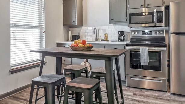 Una cocina moderna con una isla central, electrodomésticos de acero inoxidable y un ventanal con persianas.