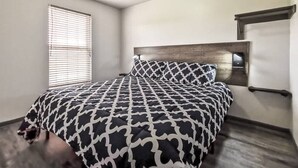 Un dormitorio con cama, cabecera, ventana con persianas y estante en la pared.