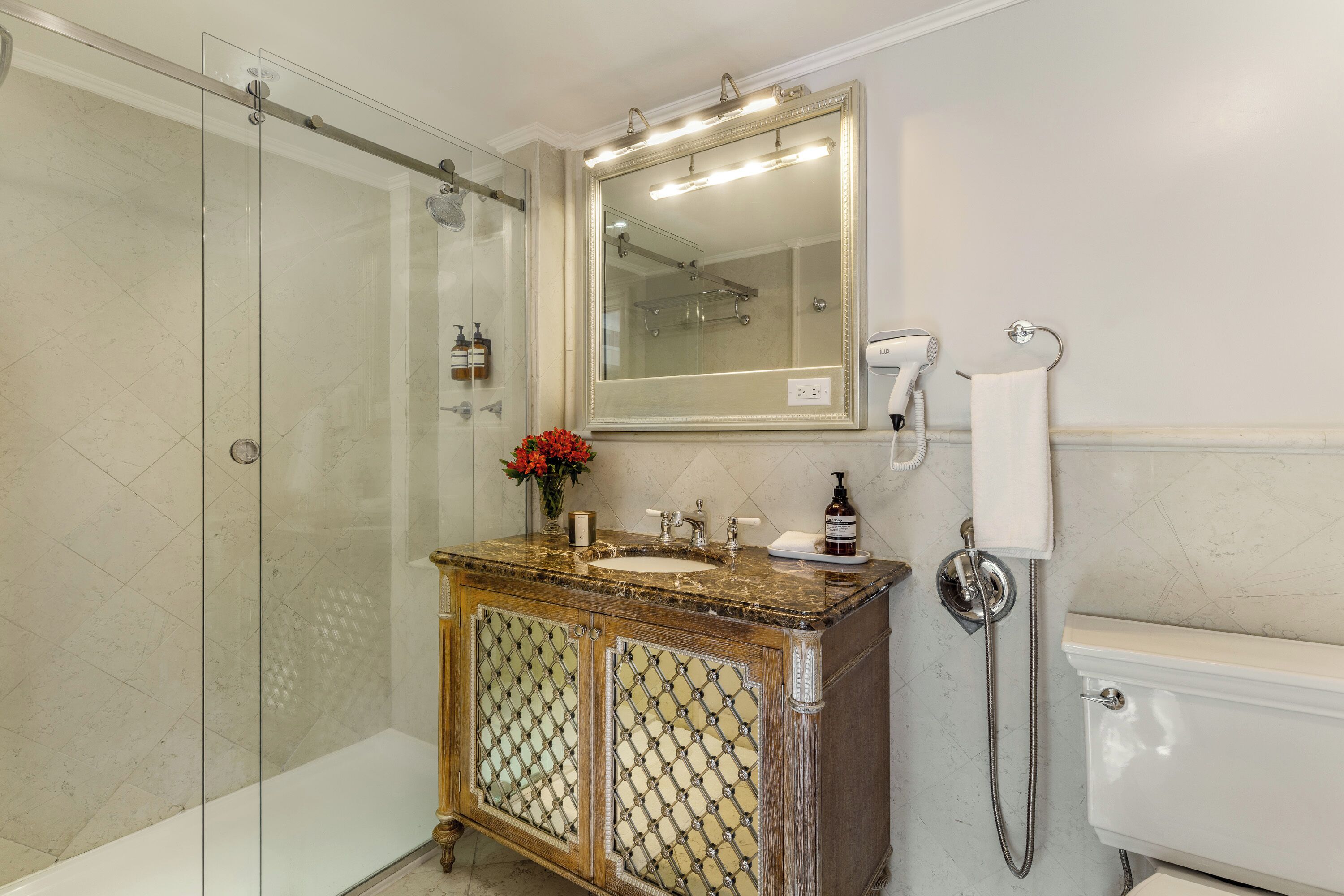 Un baño con ducha envuelta en vidrio, un lavabo con encimera de mármol, un espejo grande y una bañera blanca.