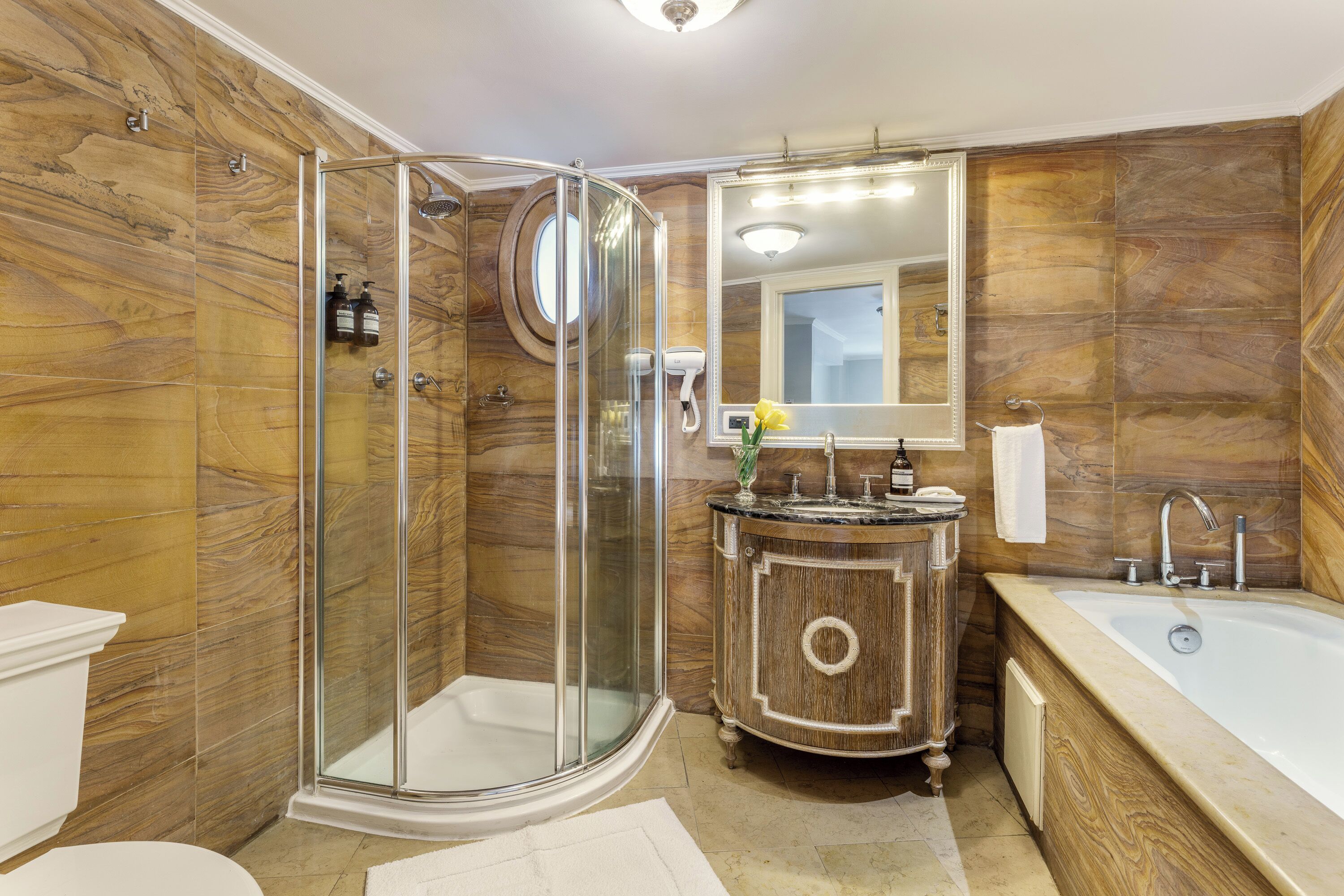 A bathroom with a glass-enclosed shower, a wooden vanity, a large bathtub, and a mirror above the sink.