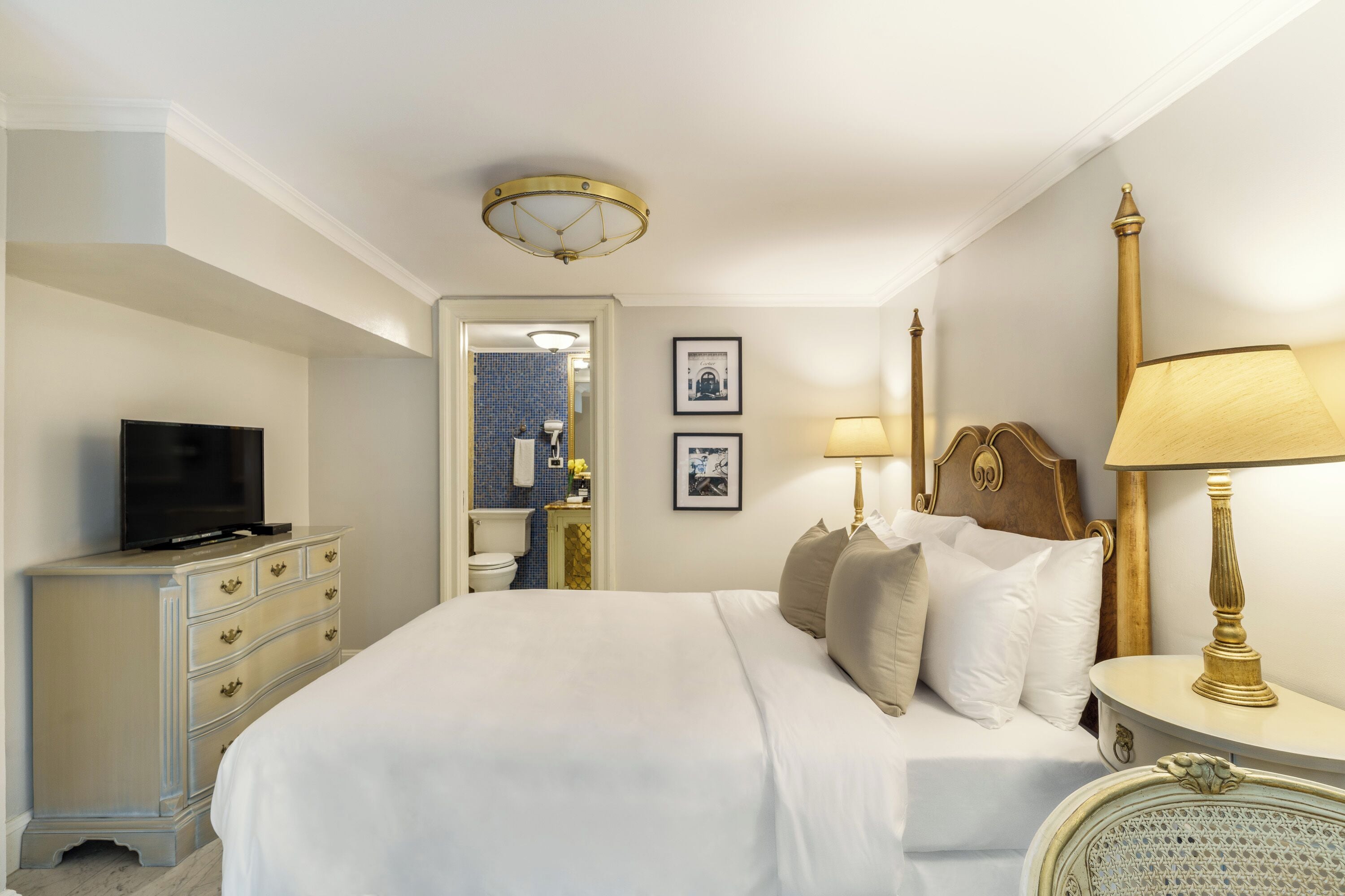 A hotel room with a bed, a dresser, a television, and a bathroom visible through an open door.