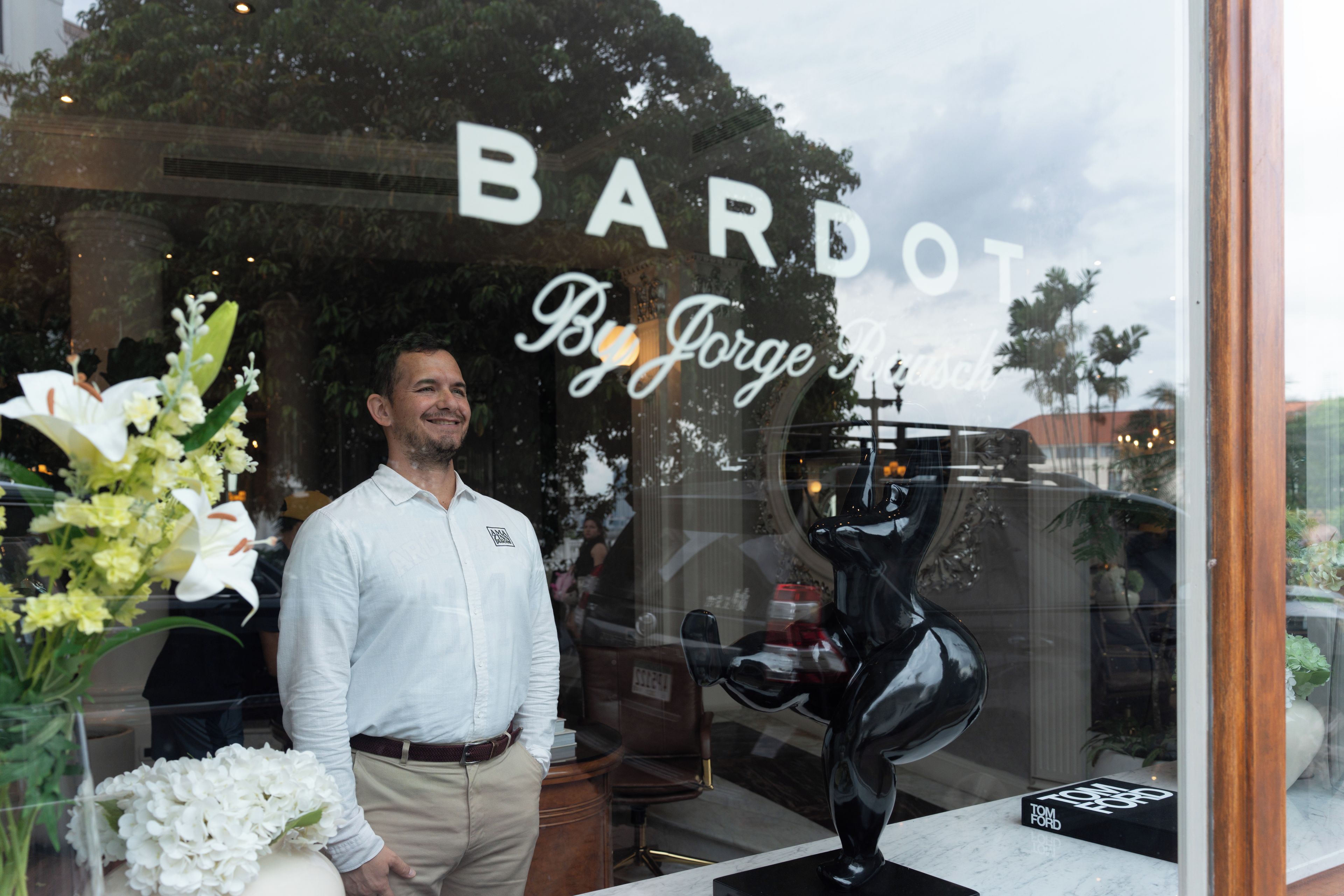 Een man staat voor een winkel met een bord waarop 'BARDOT By Jorge' staat.