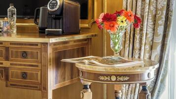 A wooden desk with a coffee maker, a vase with flowers, and a magazine.