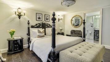 A four-poster bed with a white bedspread, a black nightstand with drawers, a black lamp, and a vase with yellow flowers.