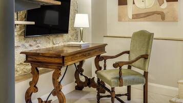 A staircase with wooden steps and metal railings, a flat-screen TV mounted on a stone wall, a wooden table with a lamp, and a green upholstered chair.