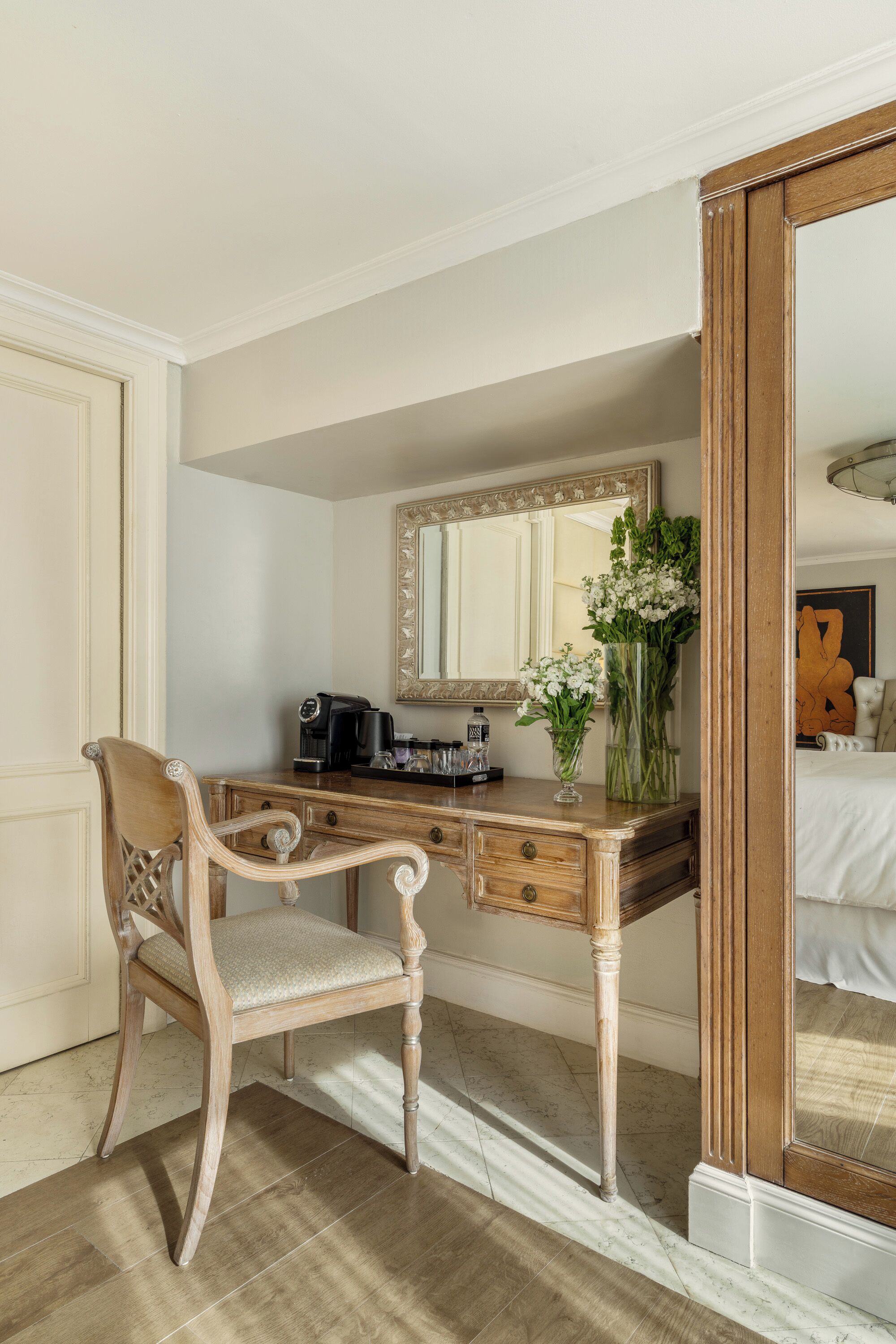 A classic wooden desk with a mirror, a chair, and a vase with flowers.