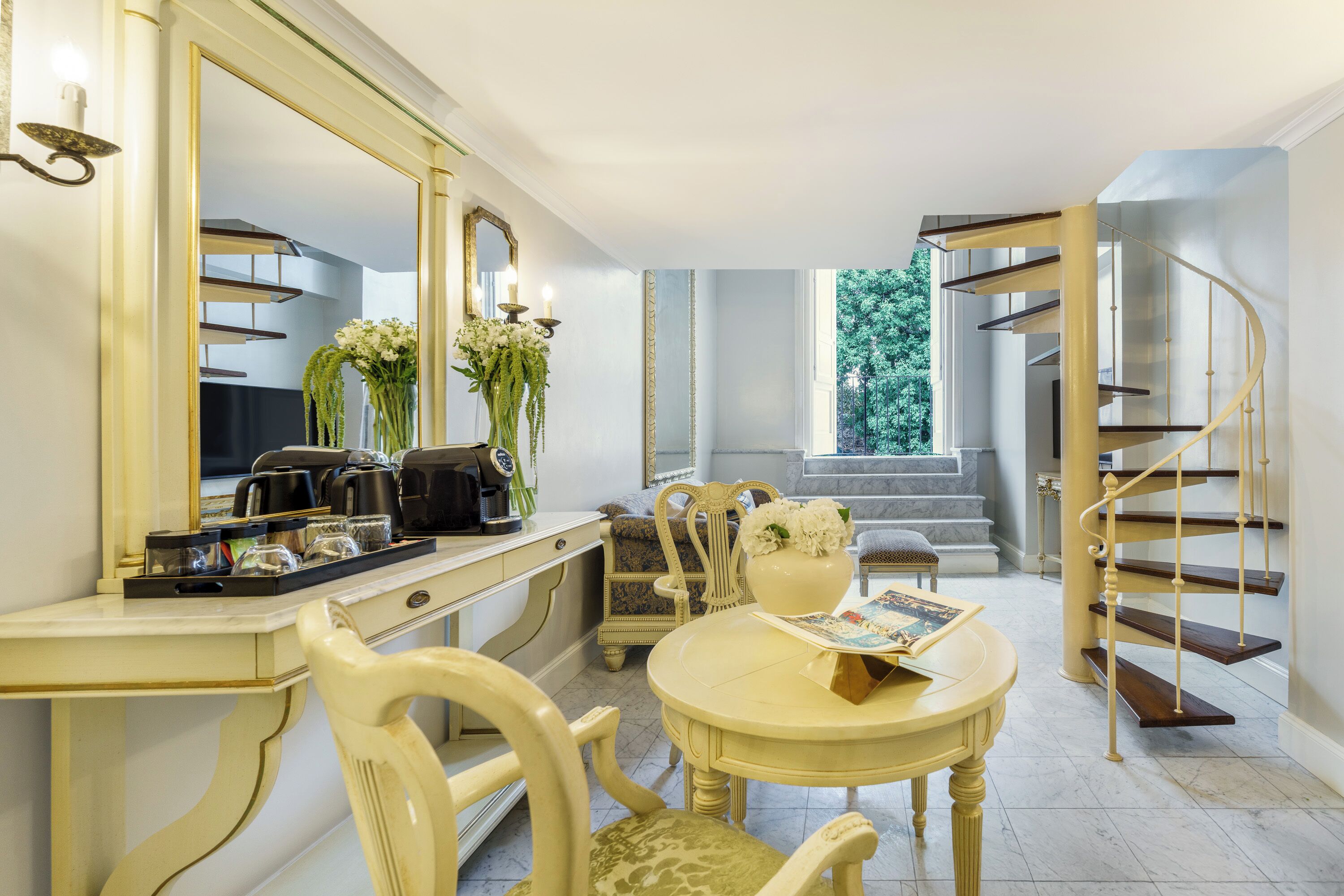 Une pièce comprenant une table à manger, des chaises, un grand miroir, une machine à café et un escalier.