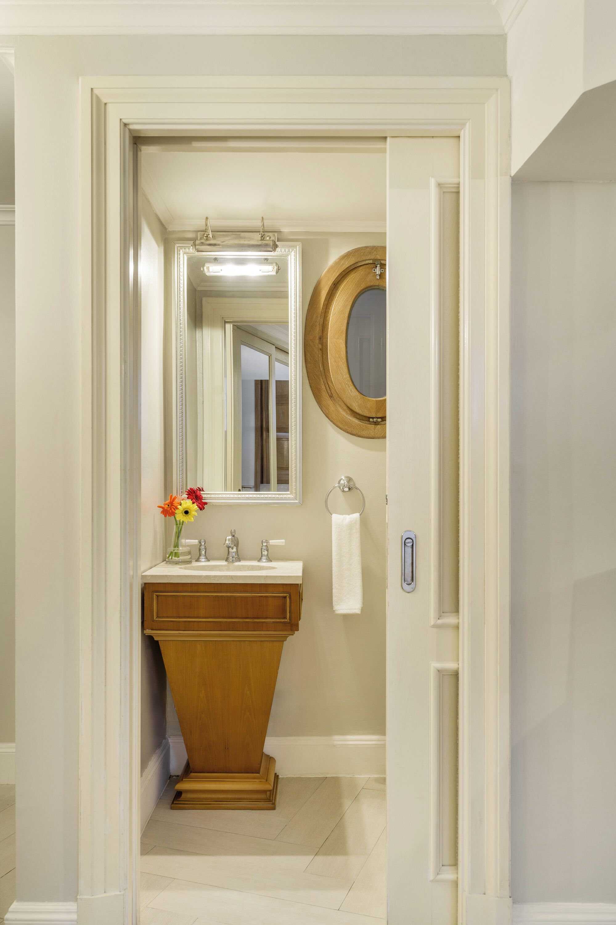 A bathroom with a wooden vanity, a mirror, a towel ring, and a vase with flowers.