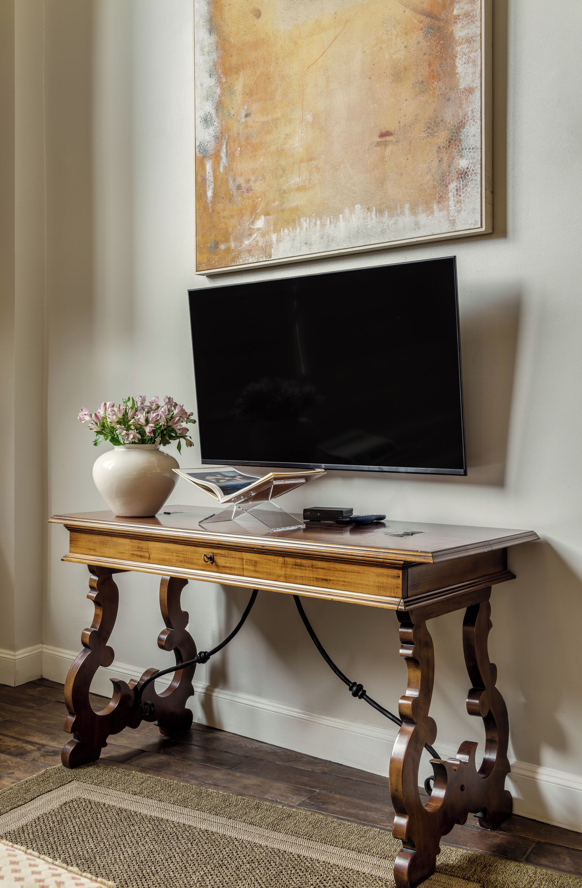 A wooden table with a vase of flowers, a remote, and a magazine.