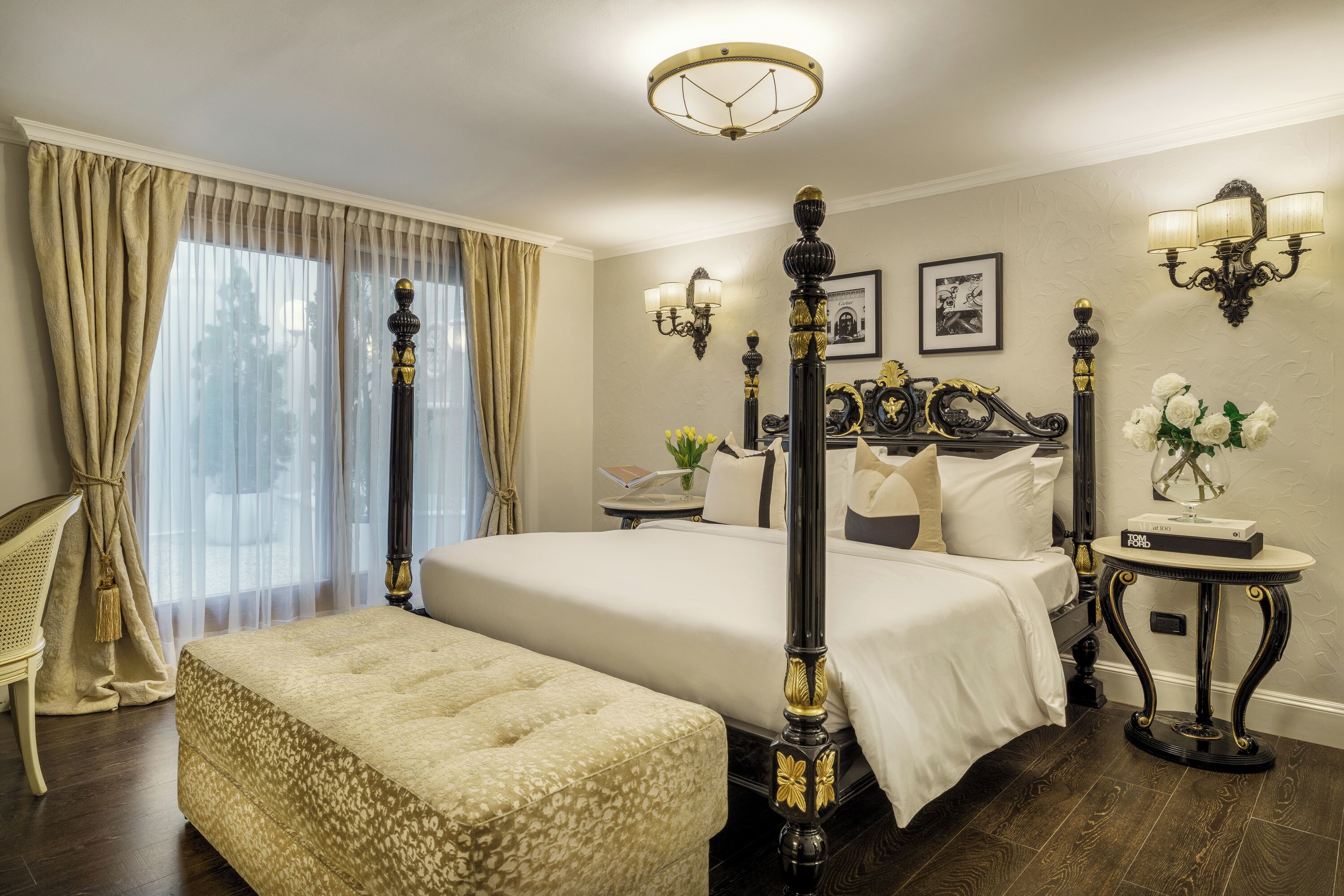 Ein Himmelbett mit Fußteil, ein Nachttisch, ein Sessel und ein großes Fenster mit Vorhängen.