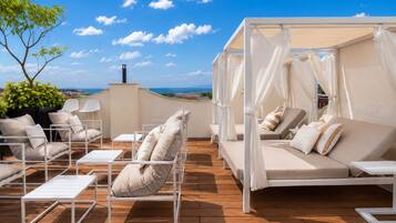 A rooftop terrace with outdoor seating, a canopy bed, and a view of the sea.