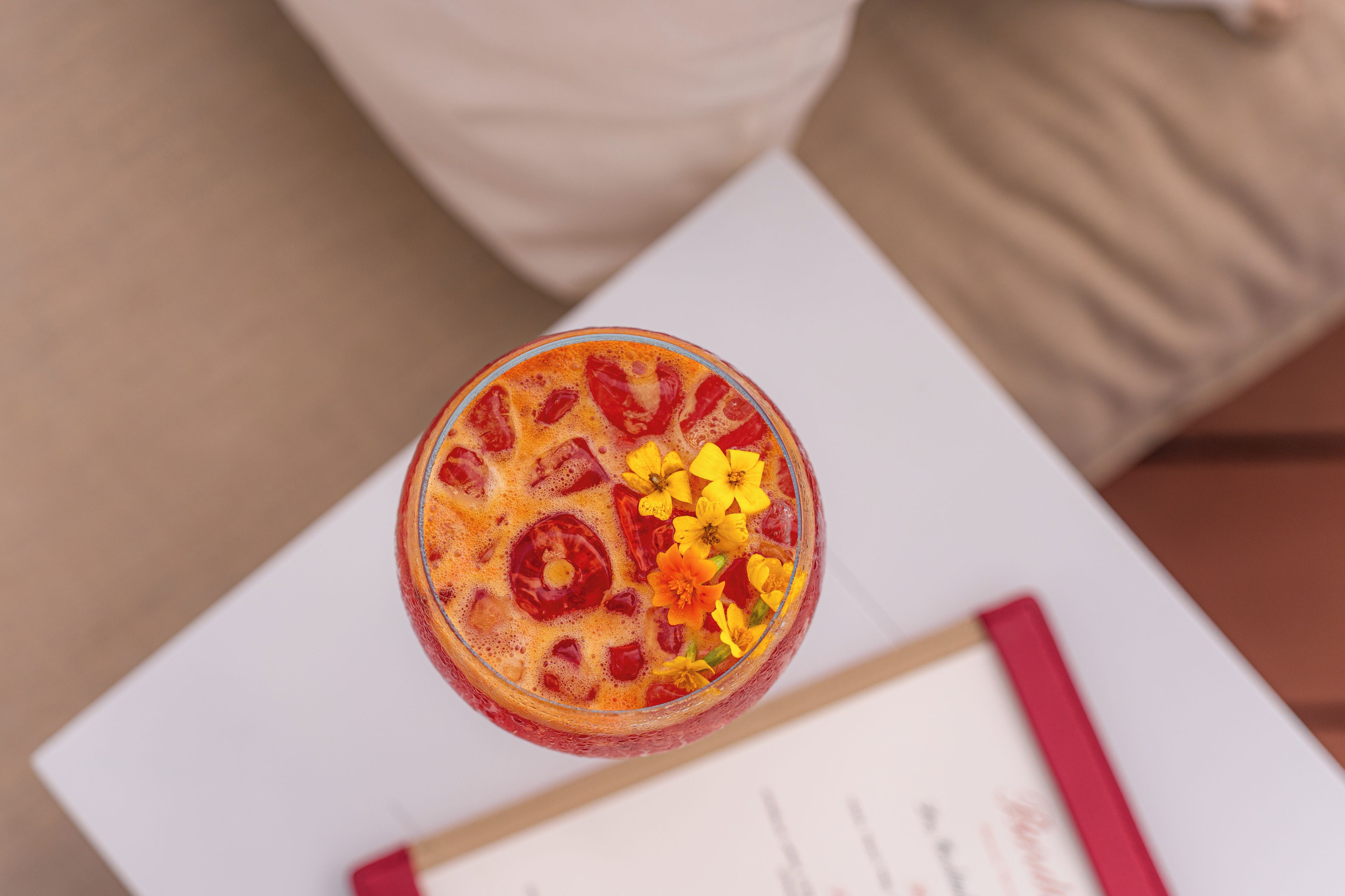 A glass of a beverage with a garnish on a white surface, possibly a table, with a document and a red pen in the background.