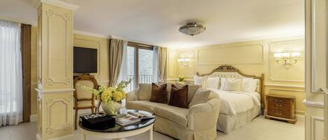 A hotel room with a bed, a sofa, a coffee table with magazines, a TV, and a nightstand.