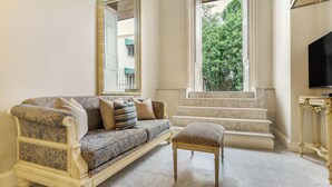 Ein Wohnzimmer mit einem gemusterten Sofa, passendem Hocker, einem großen Spiegel und einer Treppe, die in einen Außenbereich führt.