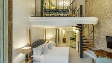 Une chambre spacieuse avec un grand lit, une table de chevet, une lampe et une commode. Un escalier mène à un niveau supérieur où se trouve un balcon.