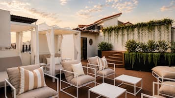 An outdoor seating area with cushioned chairs and tables, a covered seating area, and a wall with hanging plants.