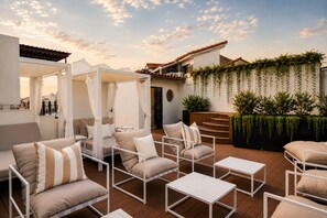 An outdoor seating area with cushioned chairs and tables, a covered seating area, and a wall with hanging plants. - Hotel Bardot Boutique (Panama City)