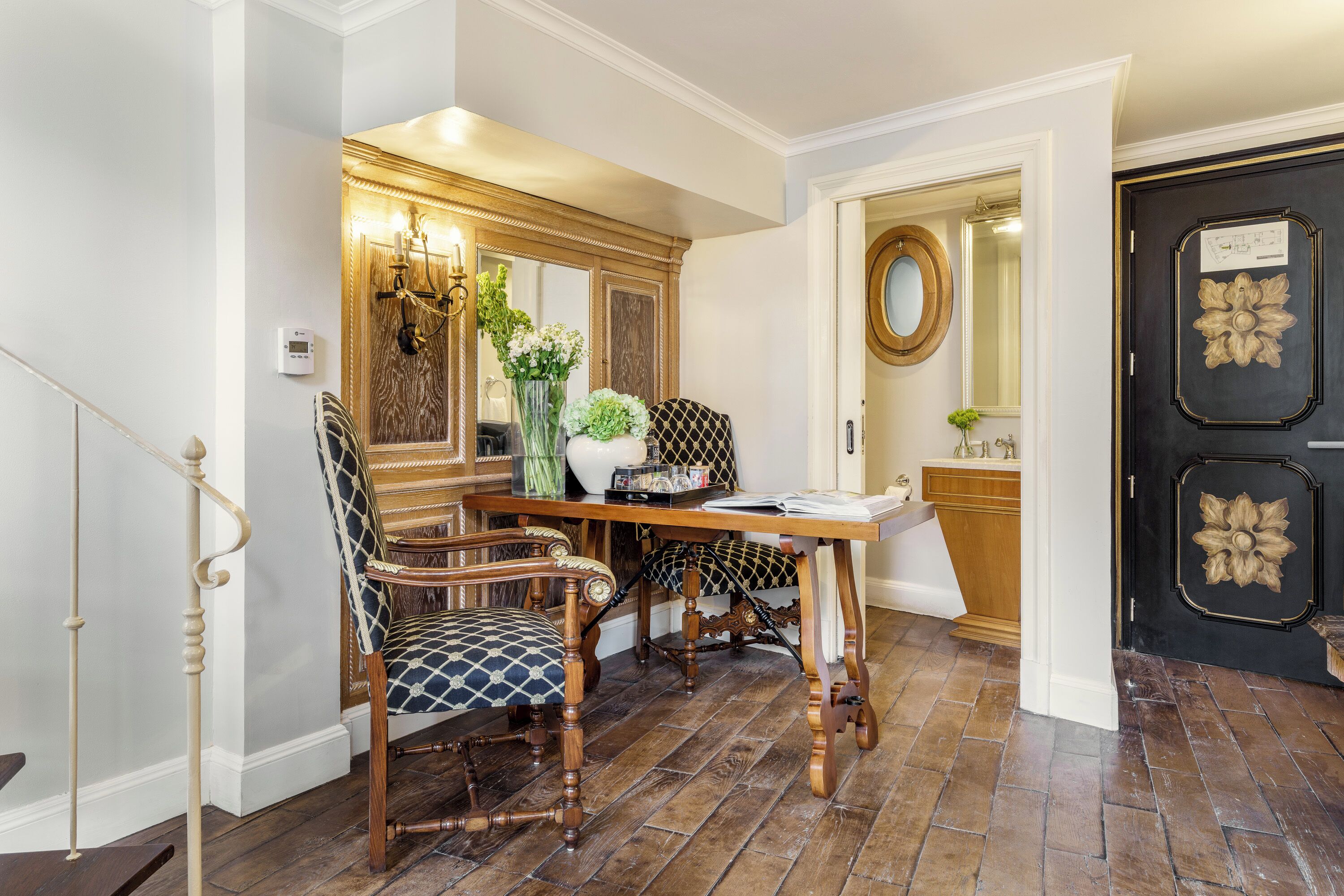 A dining area with a wooden table and chairs, a vase with flowers, and a mirror on the wall.