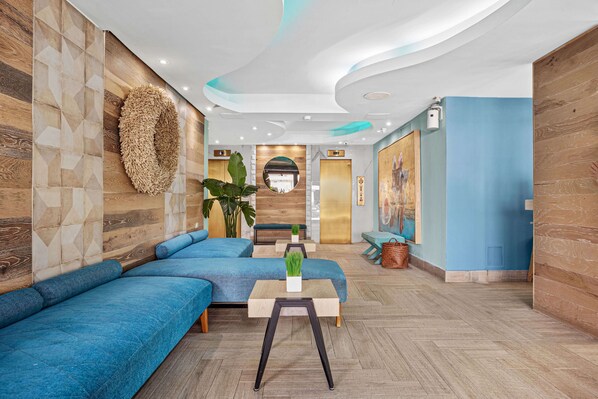 A modern hotel lobby with blue sofas, a wooden reception desk, and a large mirror on the wall. -  Abitta Condado by IHG (San Juan)