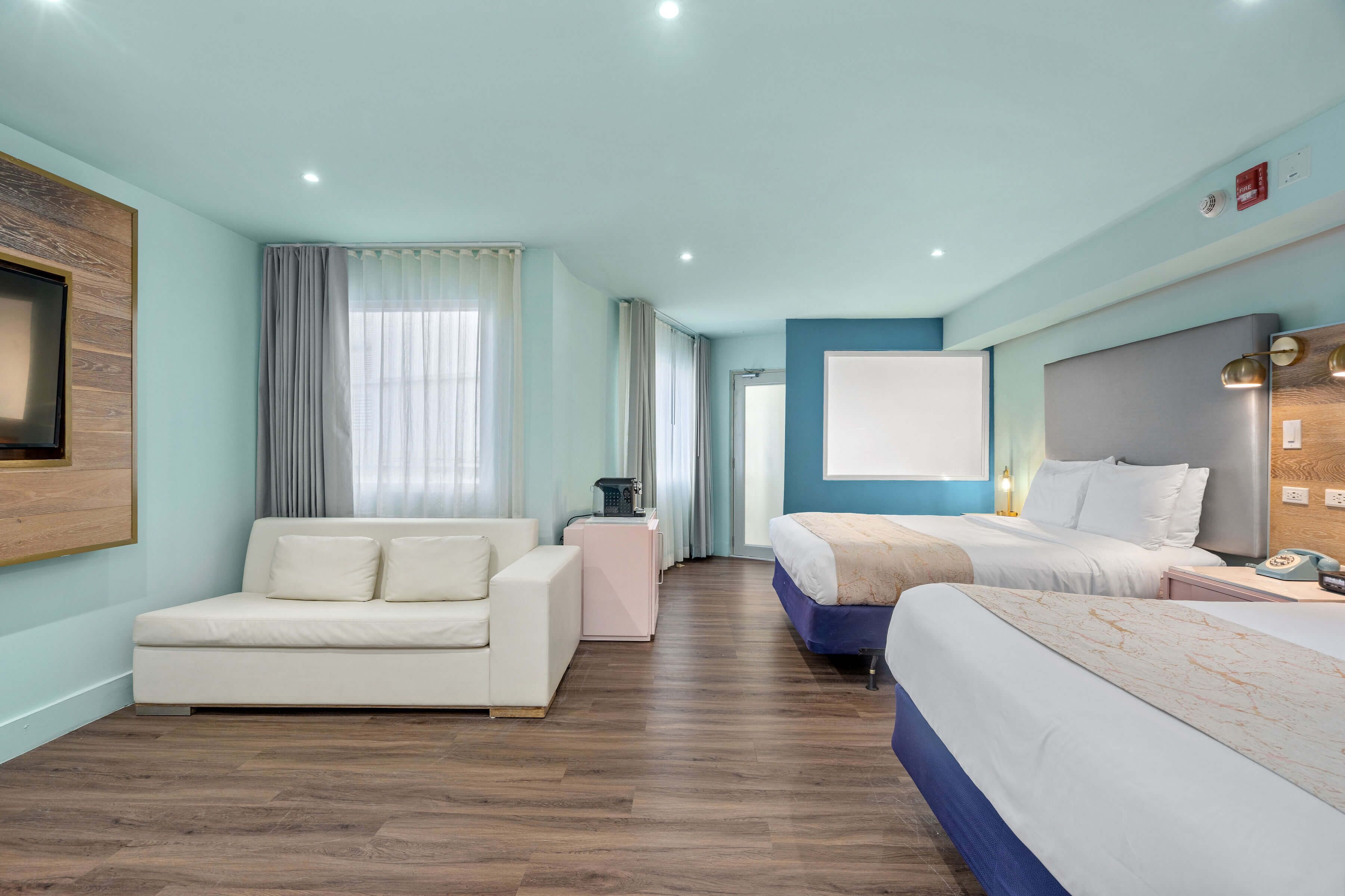 A hotel room with a sofa, a bed, a desk with a lamp, and a window with curtains.