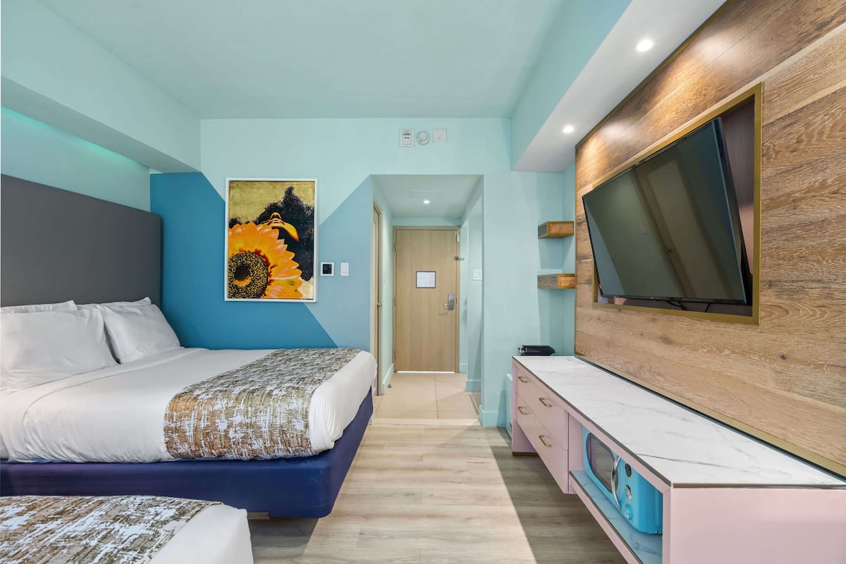 A modern hotel room with a large bed, a TV mounted on the wall, and a wooden cabinet.
