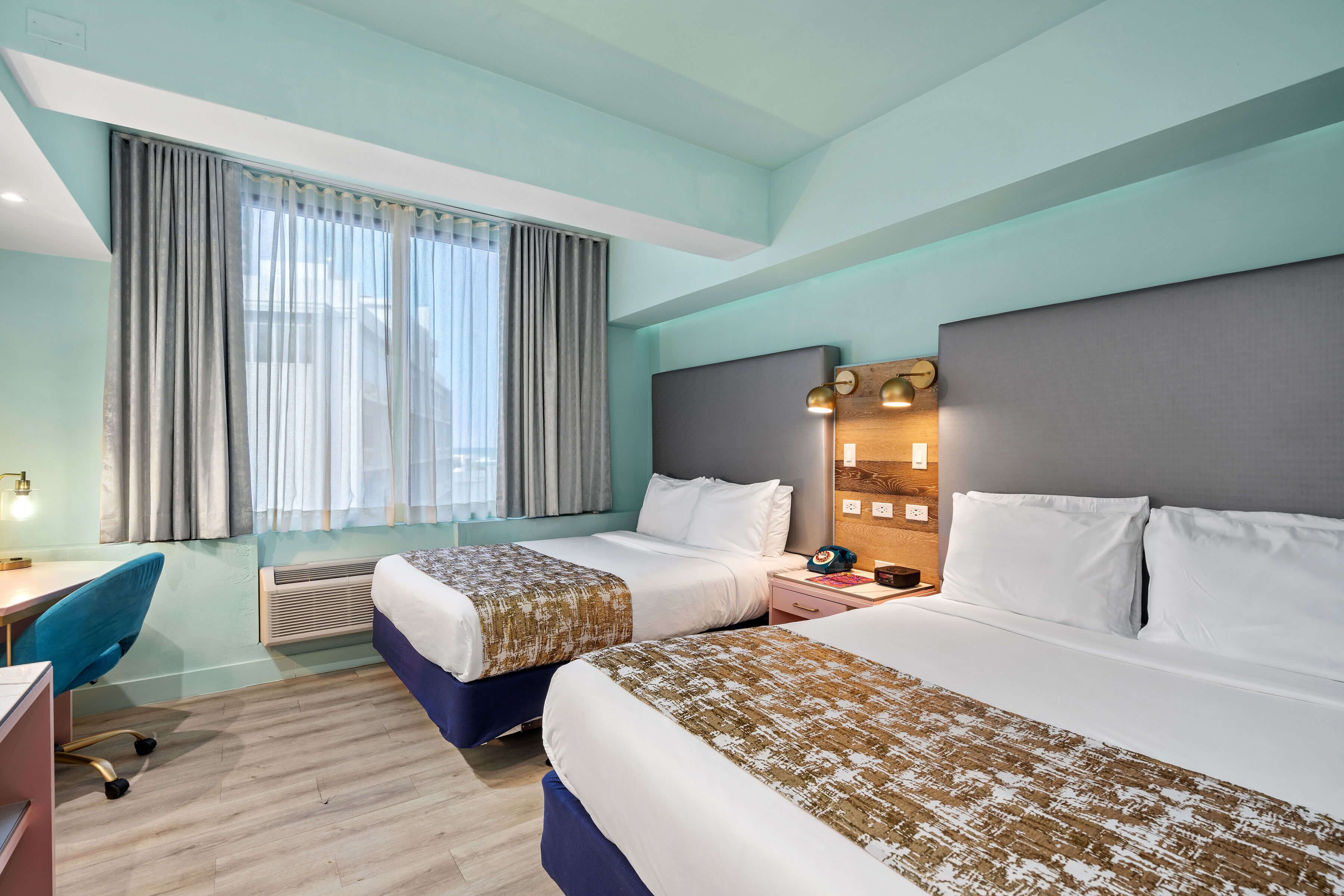 A hotel room with two beds, a desk, a chair, and a window with curtains.