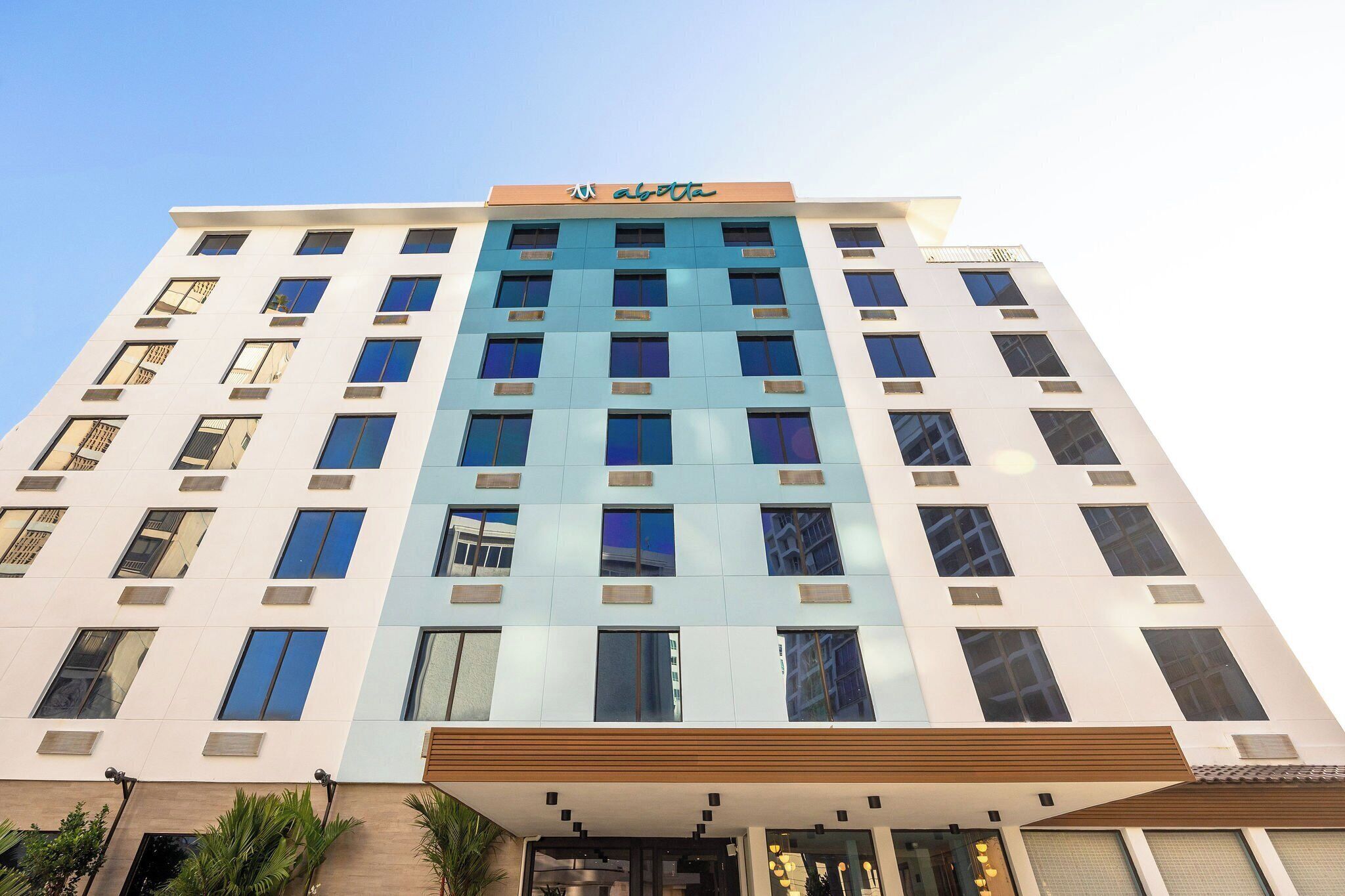 A multi-story hotel with a modern facade, featuring a prominent logo at the top.