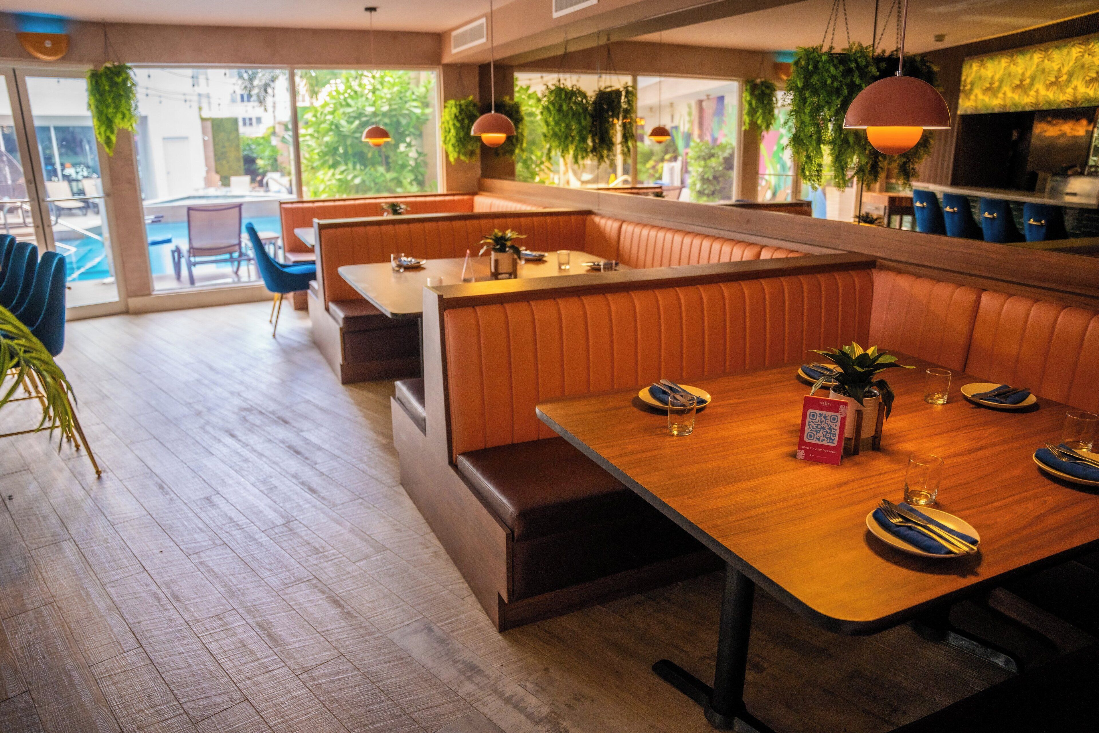 A restaurant with wooden tables and booths, large windows, and hanging plants.