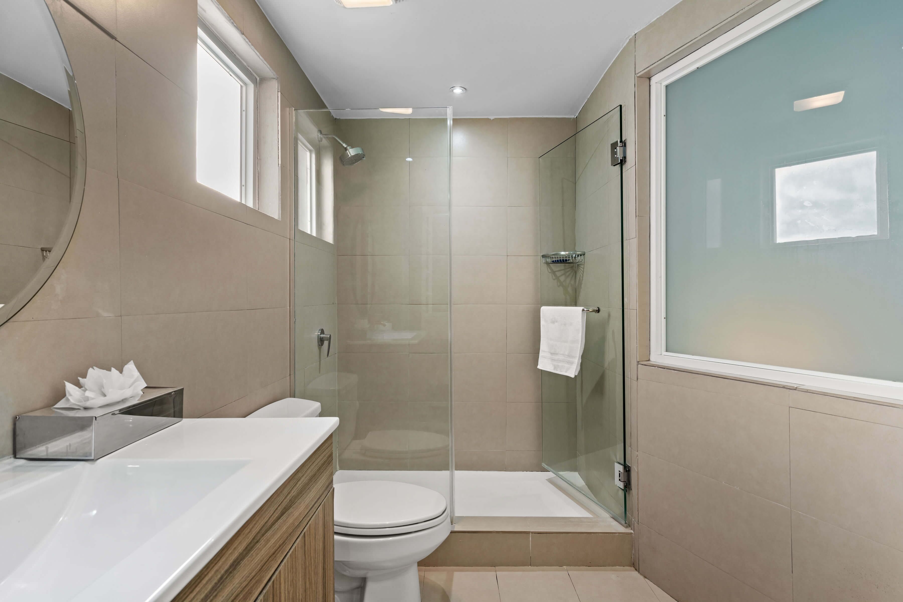 A modern bathroom with a glass shower enclosure, a white toilet, and a vanity with a mirror.
