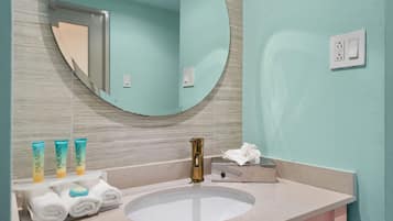 A bathroom with a round mirror, a sink, and toiletries.