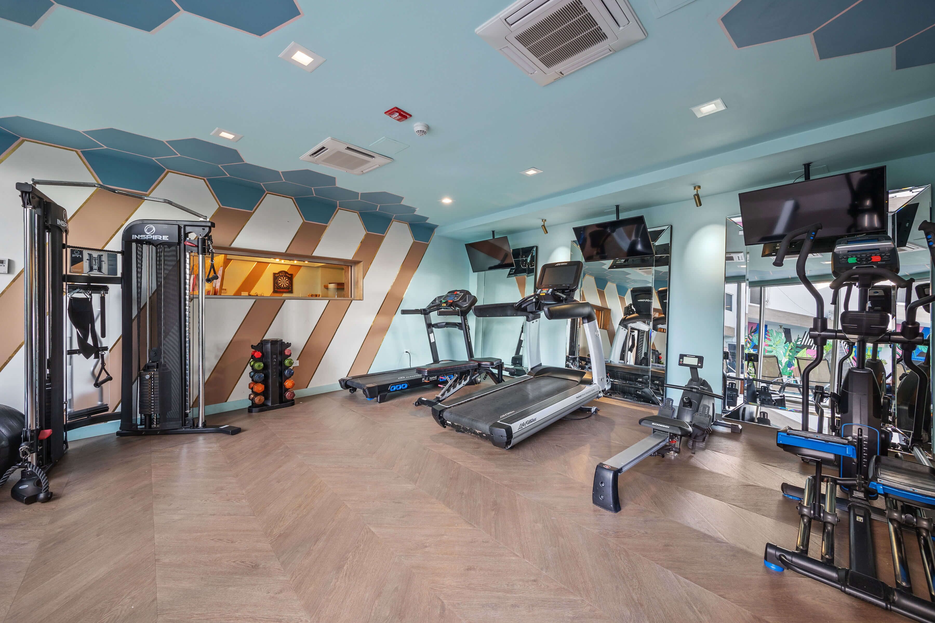 Un gimnasio con cintas de correr, máquinas de pesas y un espejo grande.