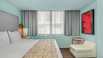 A hotel room with a large bed, a bedside table with a lamp, a small sofa, a window with curtains, and a red abstract painting on the wall.