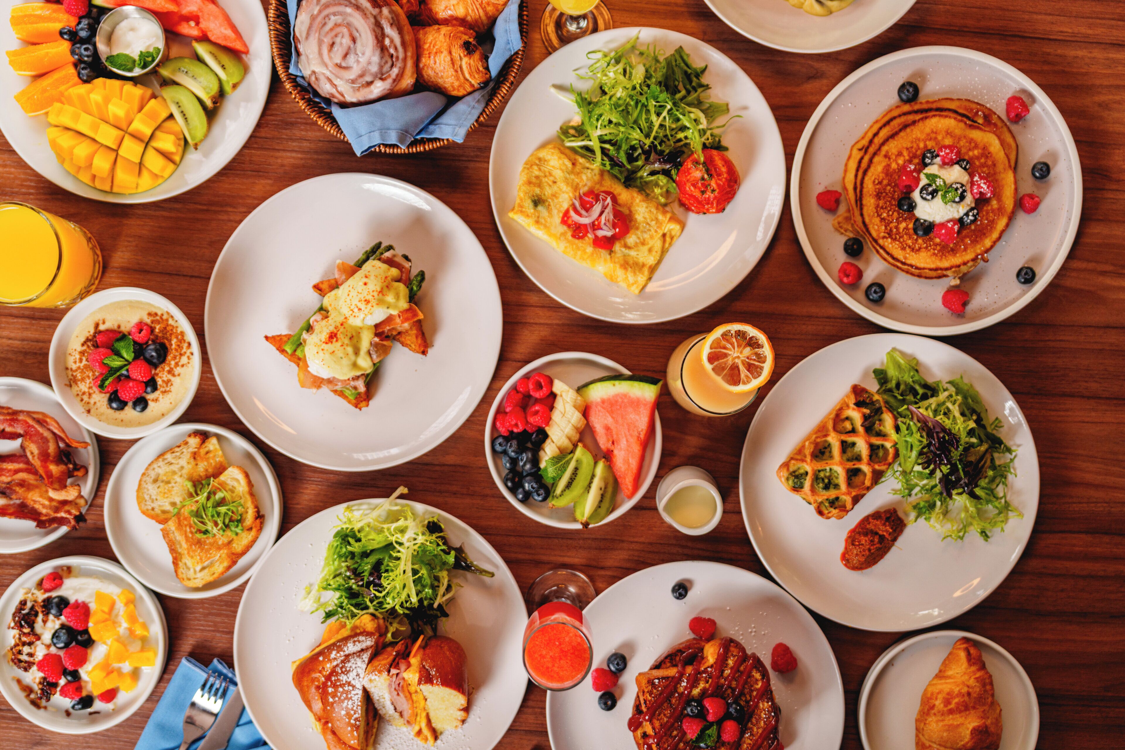 A variety of breakfast dishes on plates, including pancakes, omelets, and pastries.