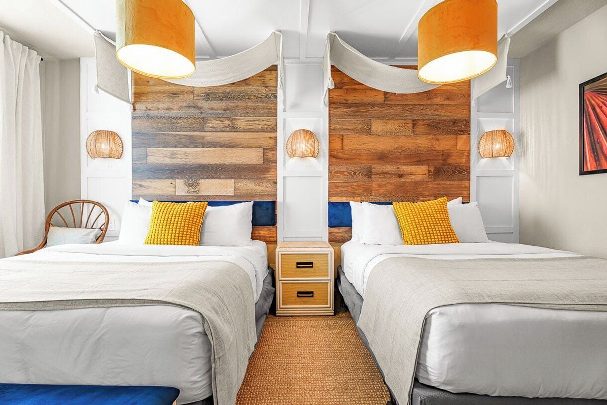 A hotel room with two beds, a wooden accent wall, and a woven rug.