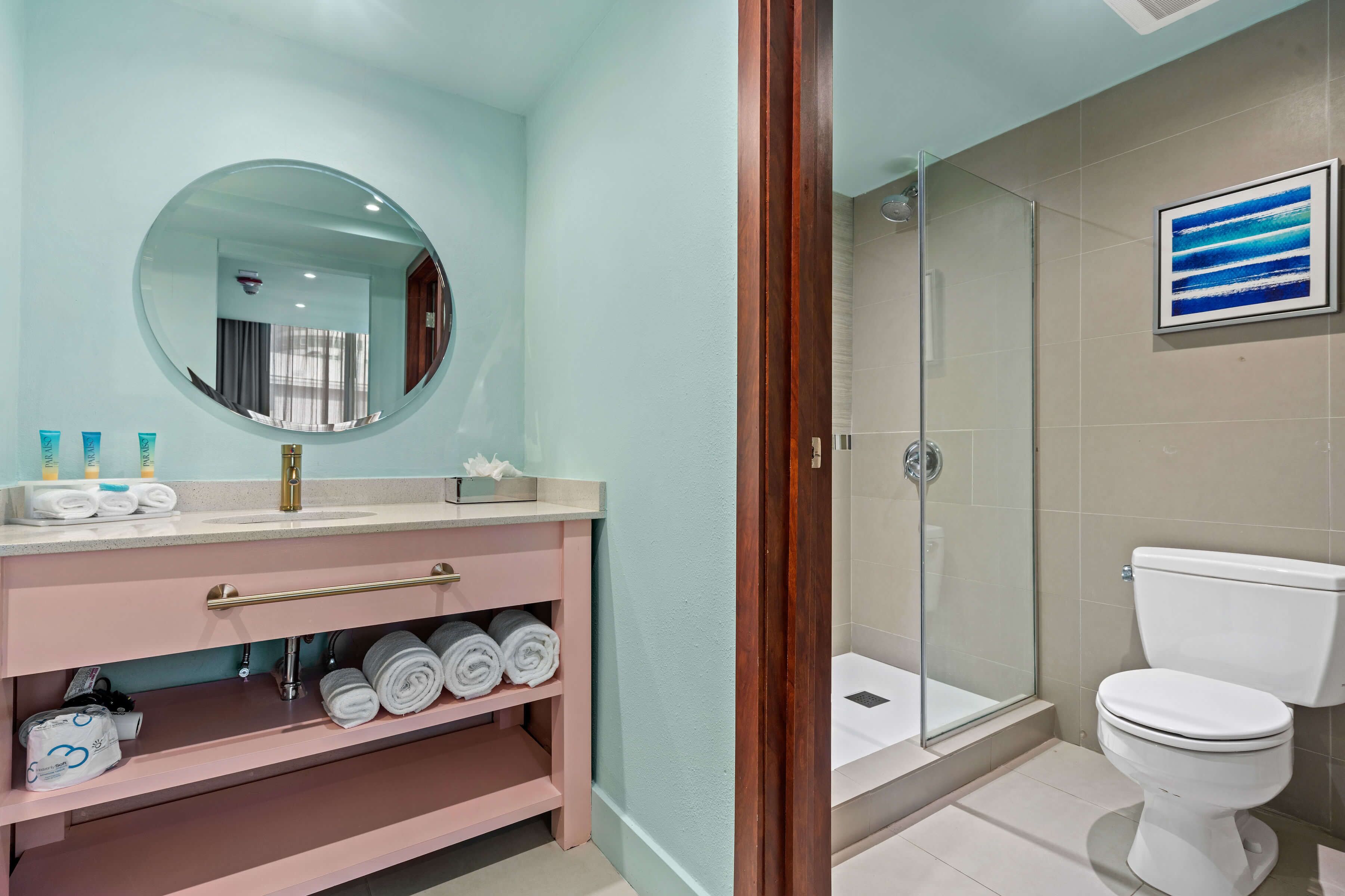 Ein Badezimmer mit rundem Spiegel, Waschbecken mit Toilettenartikeln, Toilette und einer Duschkabine.