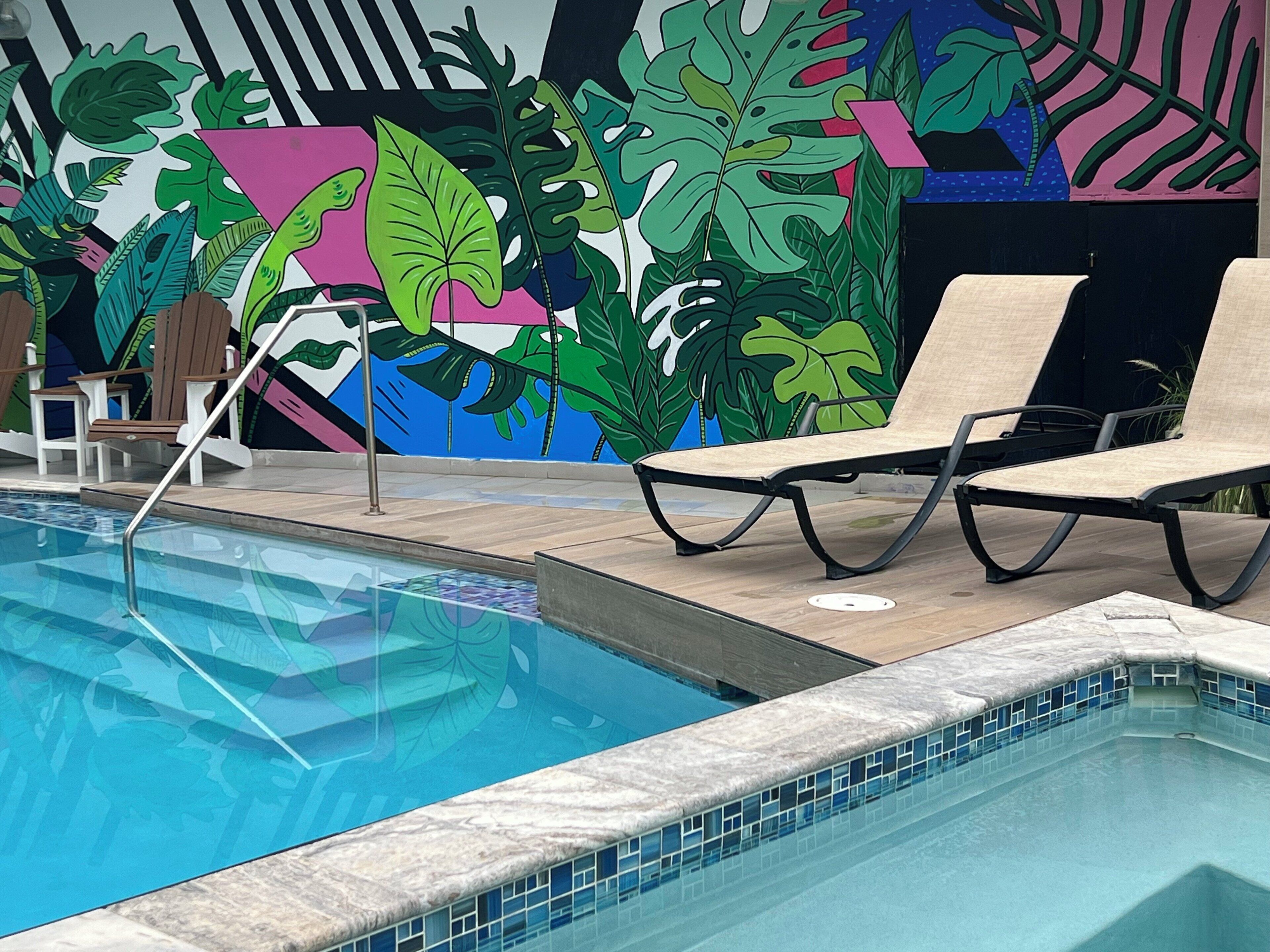Une piscine dotée de chaises longues et ornée d’une fresque représentant des feuilles tropicales.