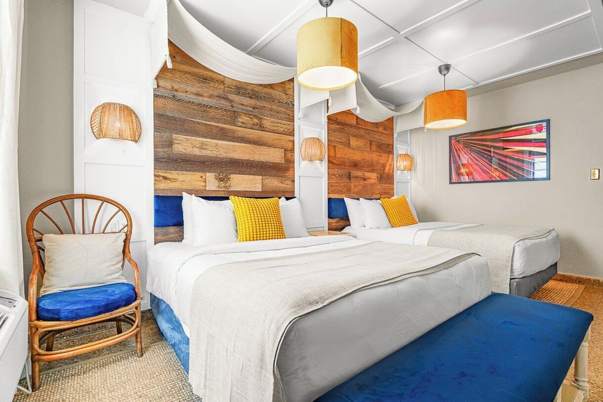 Habitación de hotel con dos camas, una silla de mimbre y un cuadro abstracto grande en la pared.