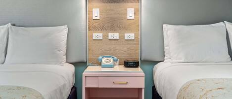 A hotel room with two beds, a nightstand with a phone and a clock, and wall-mounted lighting.