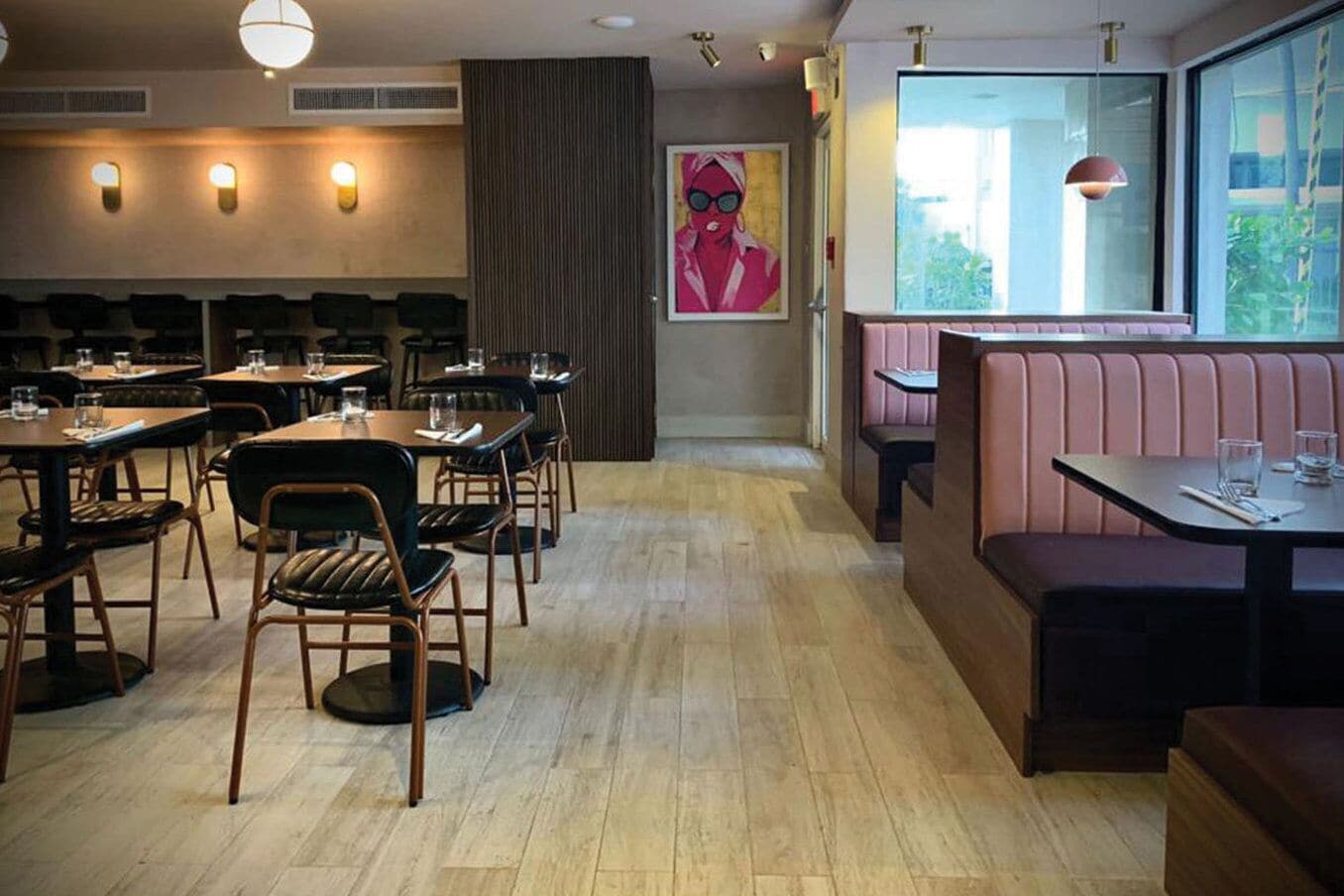 A restaurant with wooden flooring, booths, and tables. There is a large window on the right side.