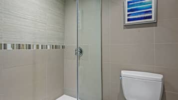 A bathroom with a glass shower enclosure, a white toilet, and a framed abstract painting on the wall.