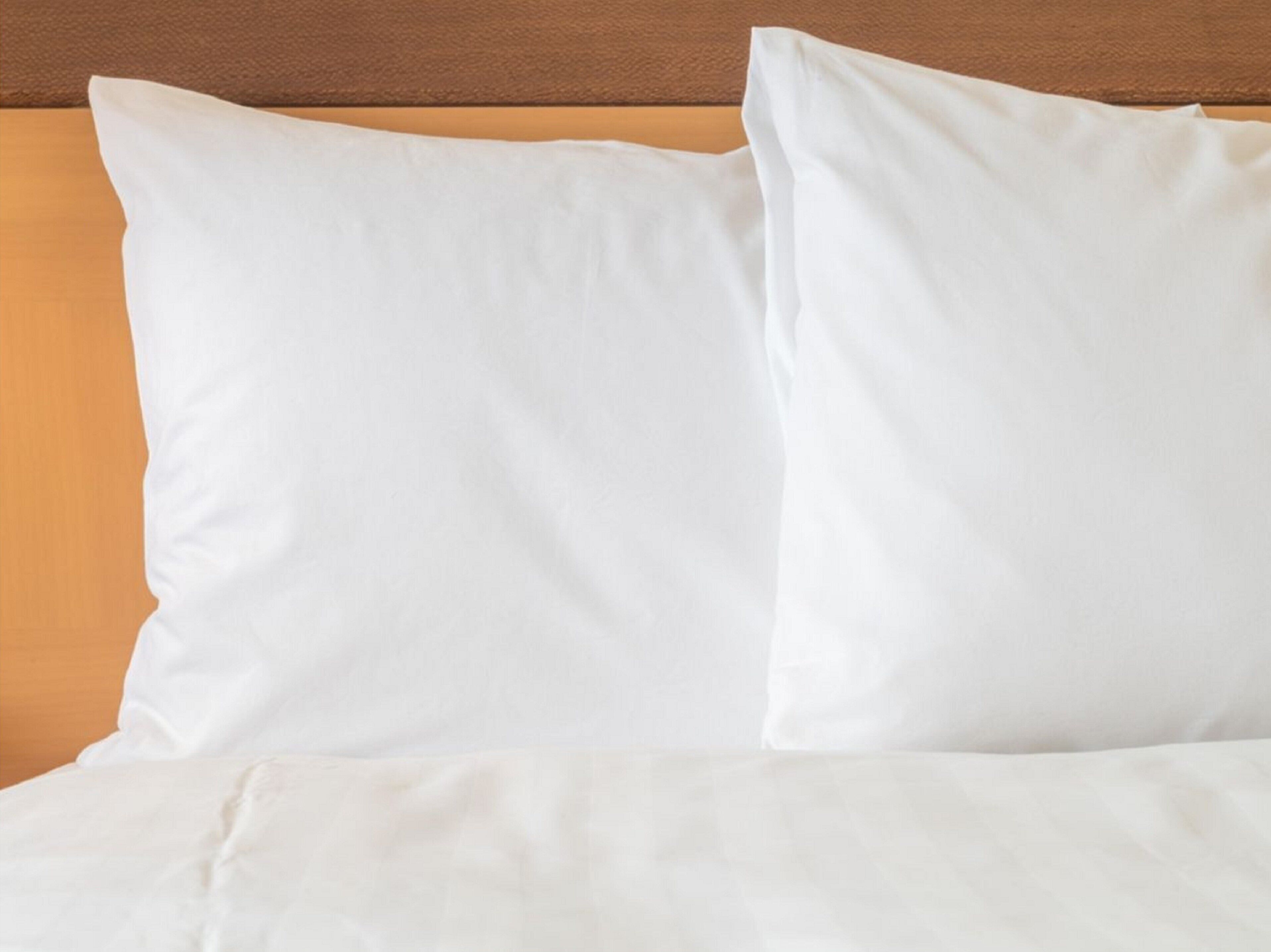 A bed with white bedding and pillows against a wooden headboard.