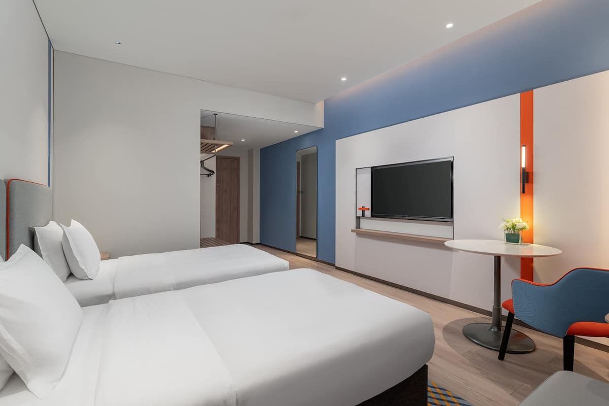 Una habitación de hotel moderna con dos camas, un televisor, una mesita pequeña y una silla.