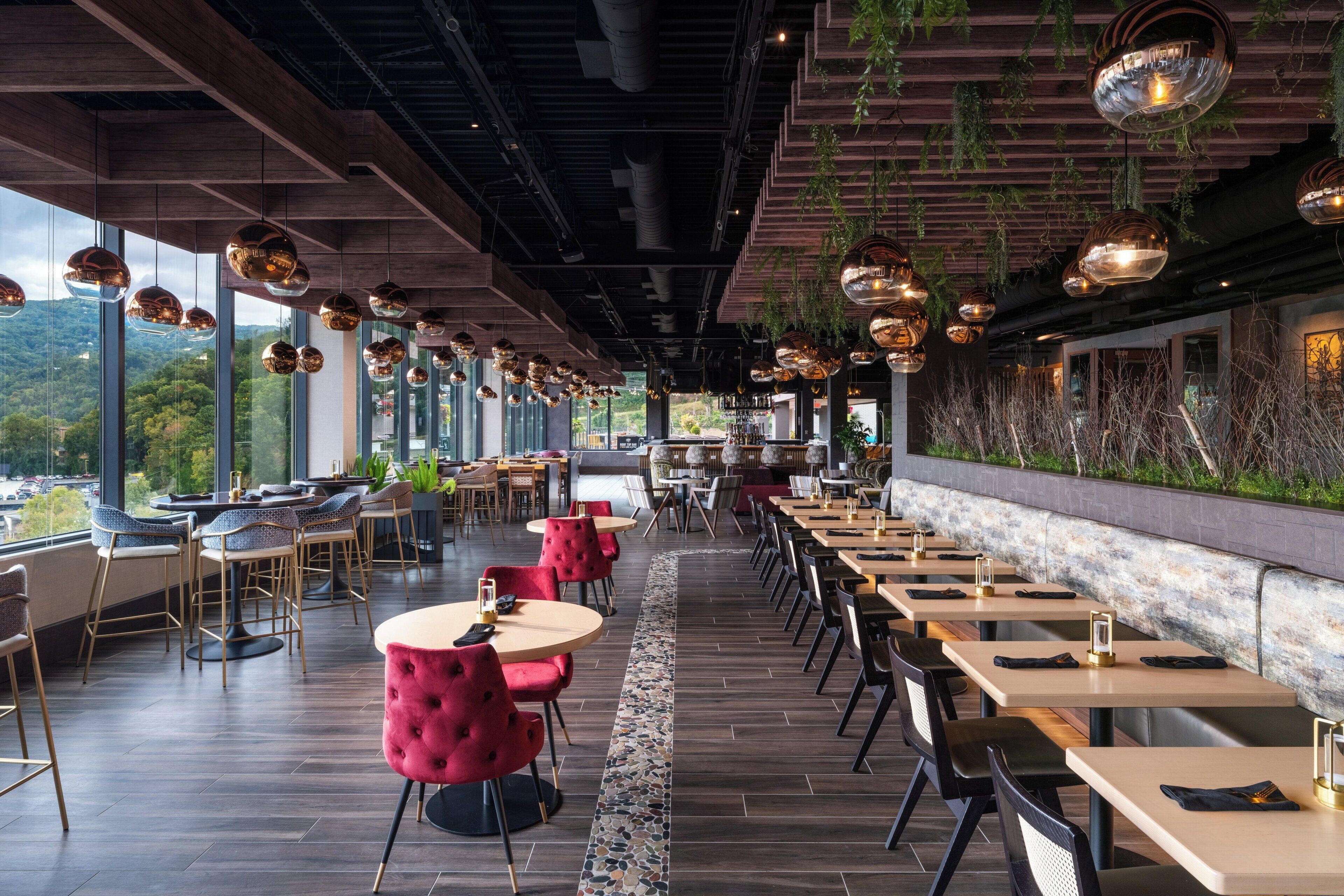 A modern restaurant with long communal tables, individual booths, and hanging pendant lights.