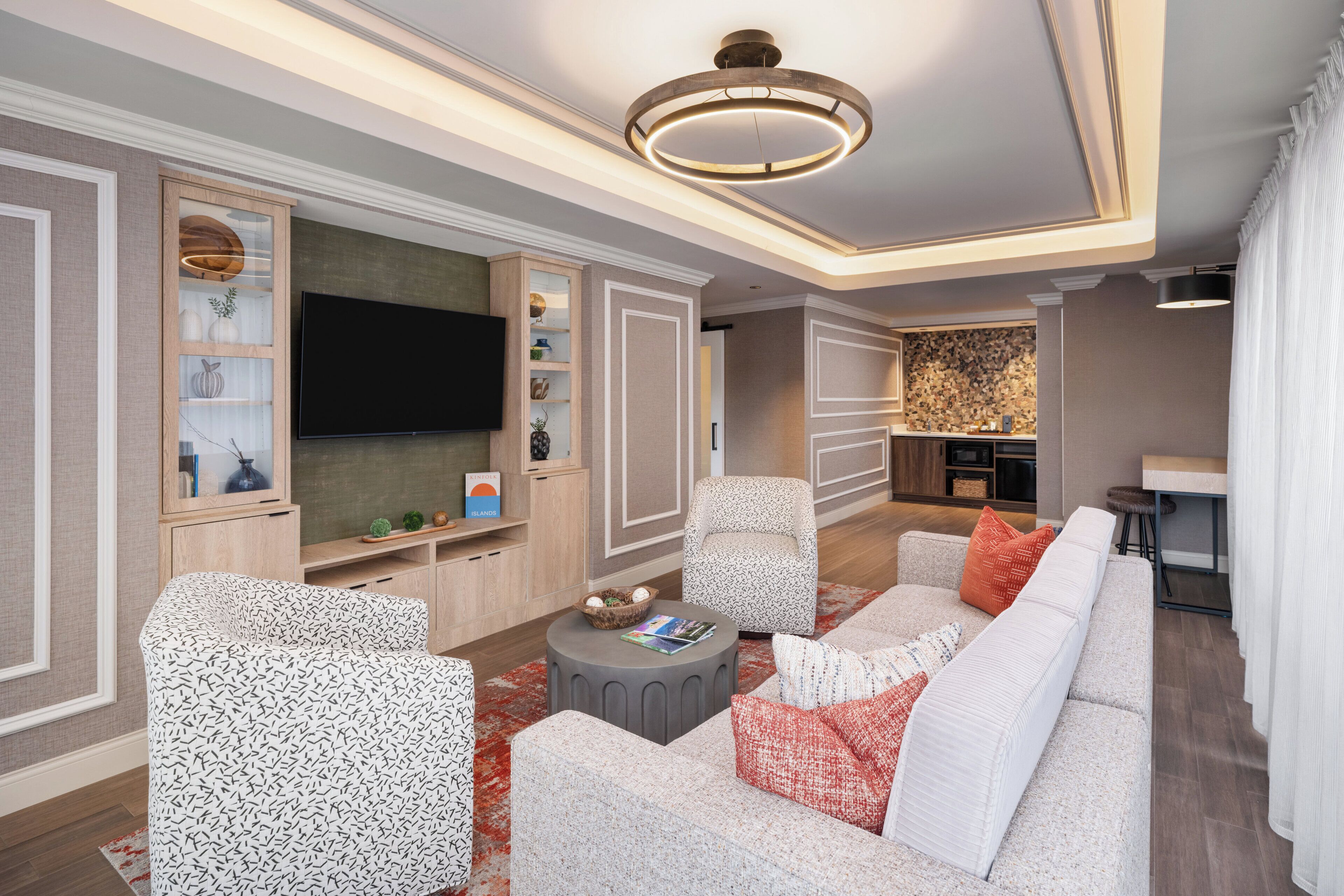 A modern living room with a flat-screen TV, patterned sofas, a round coffee table, and built-in shelving.