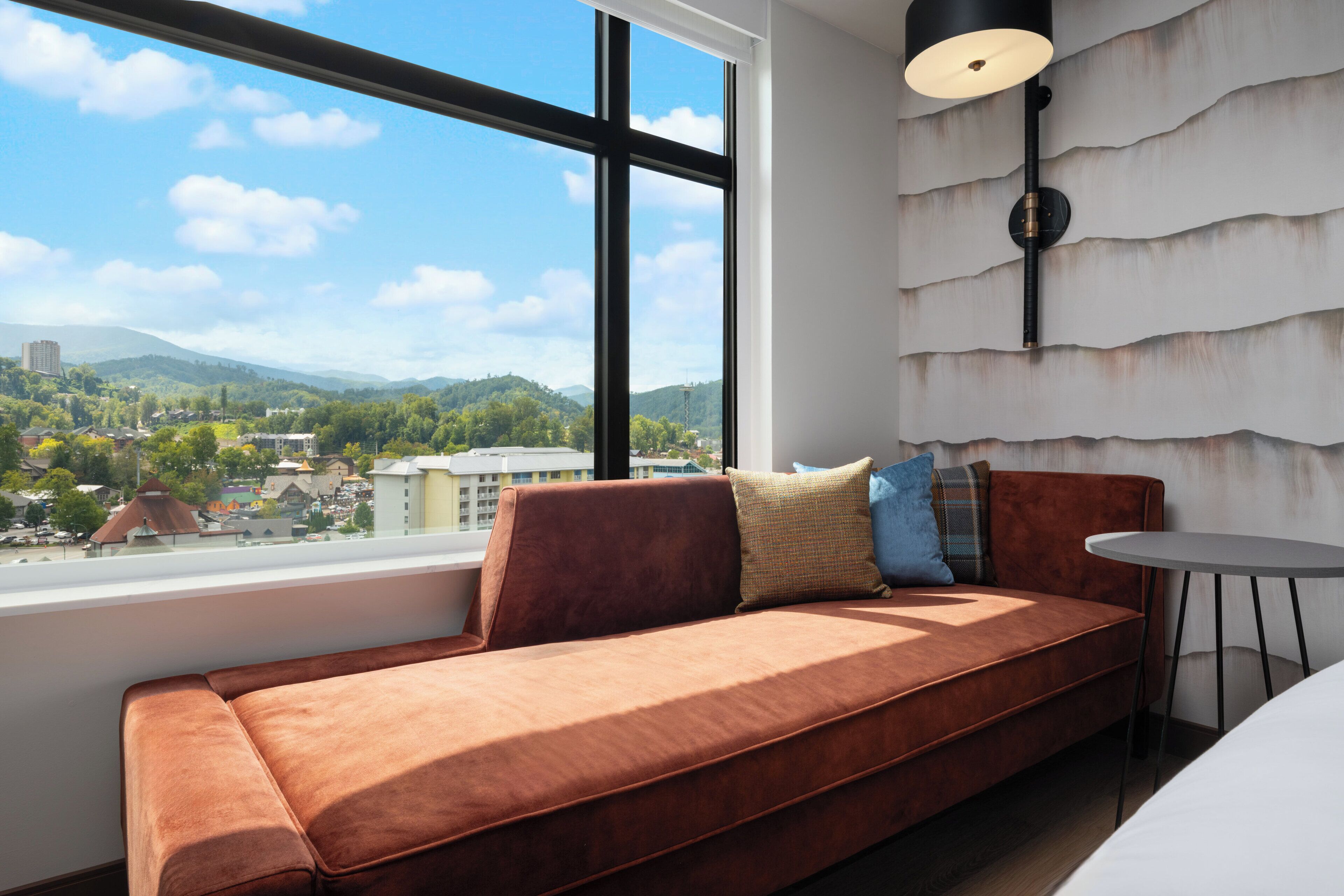 A modern room with a large window, a brown sofa, a small table, and a wall-mounted lamp.