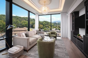 Un moderno salón con un ventanal grande, un sofá, un sillón verde y un televisor de pantalla plana.