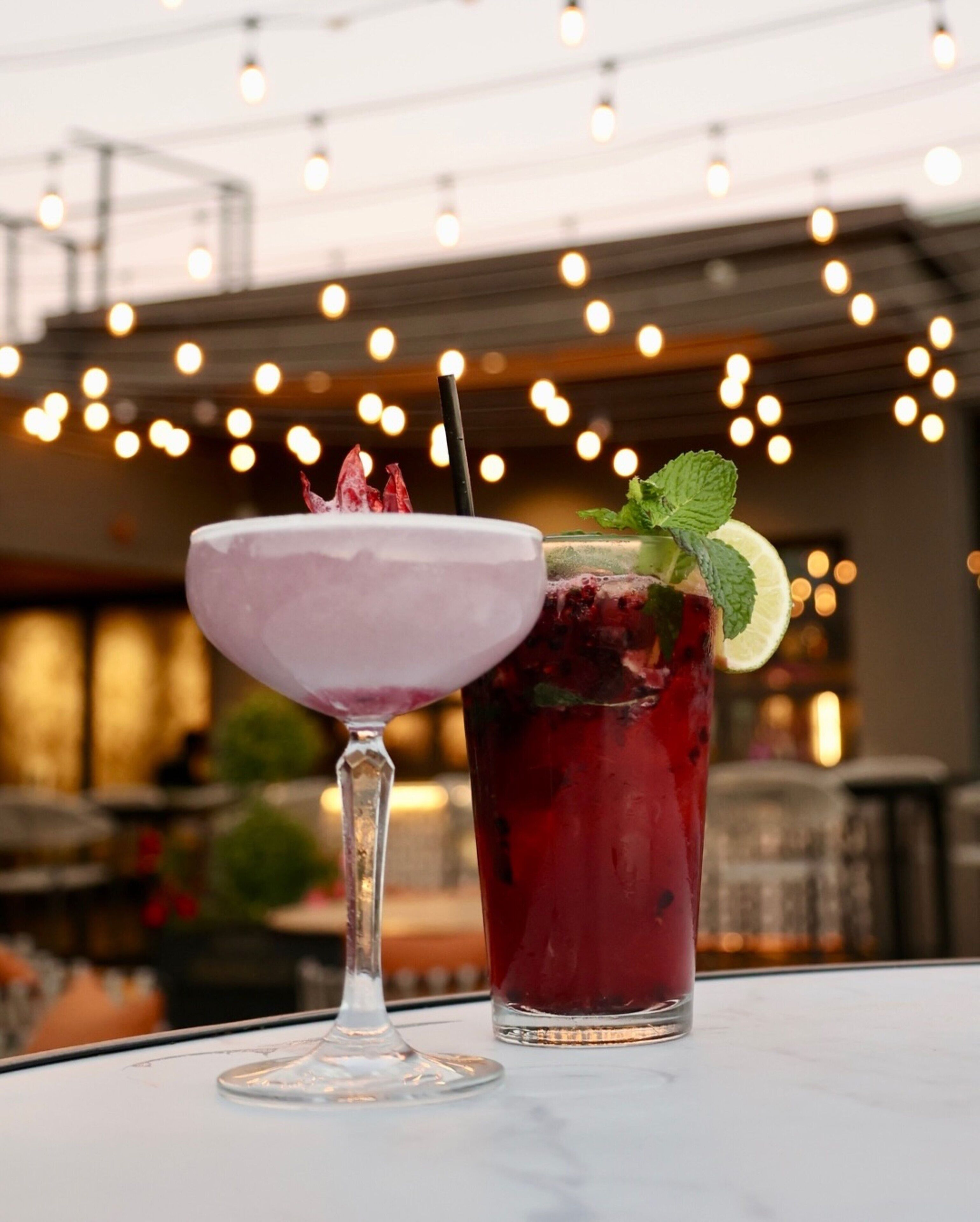 Two drinks on a table with a blurred background of lights and a bar.